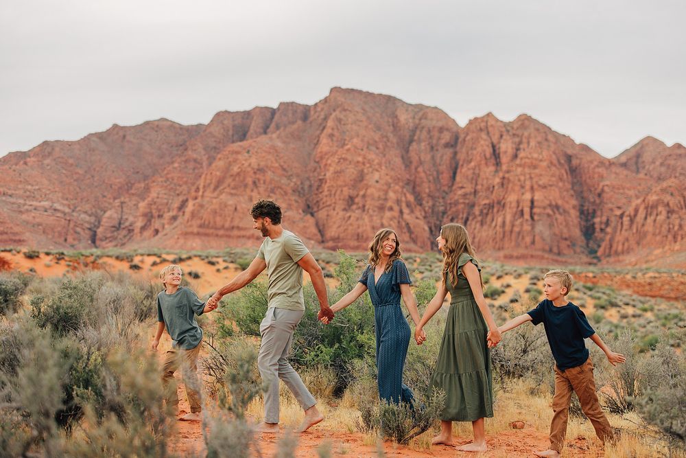 Family holding hands walking through red rock desert landscape with stunning sandstone cliffs in background.