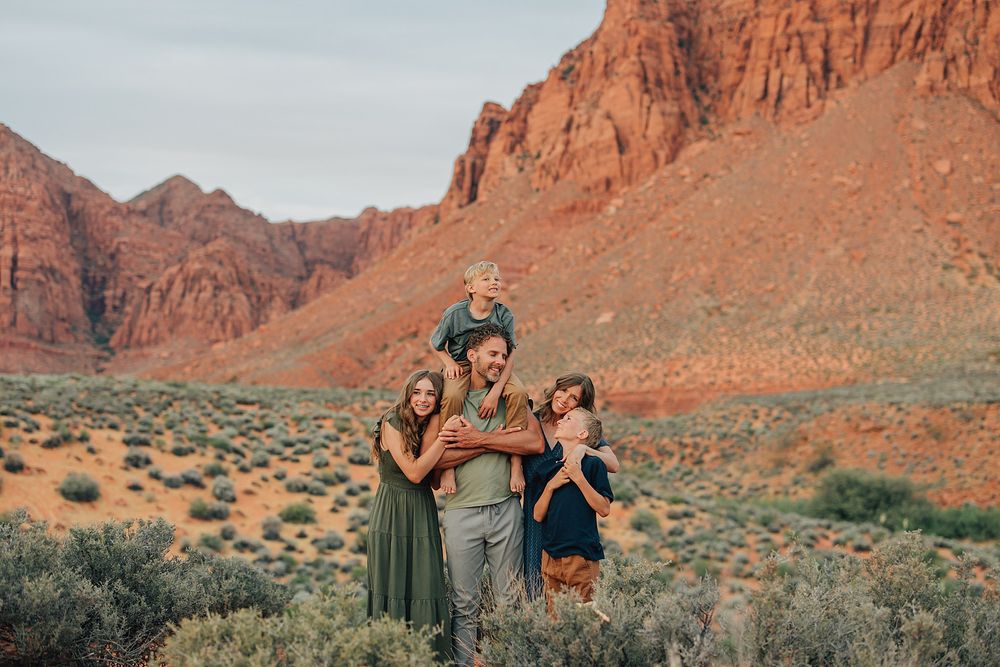 Family of five posing happily in a red rock desert canyon landscape at golden hour.