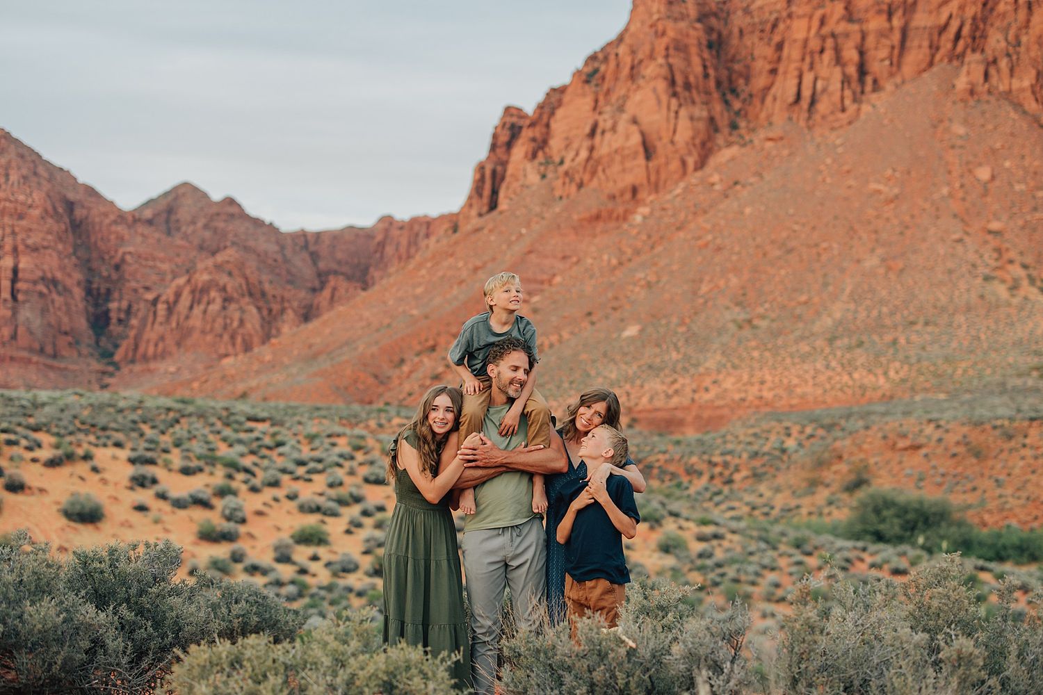 Family of five posing happily in a red rock desert canyon landscape at golden hour.