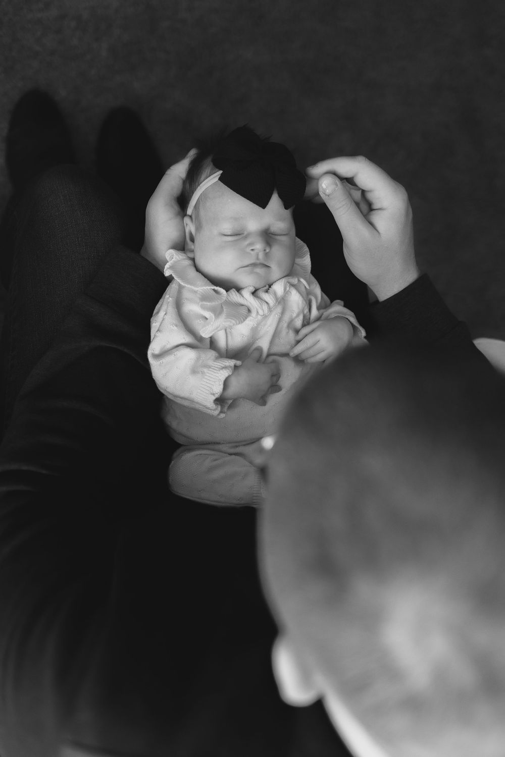 Black and white photo of a newborn baby sleeping peacefully in a parent's hands.