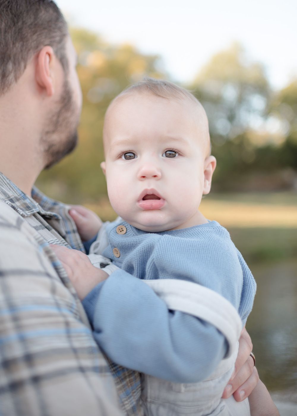 Father holding baby boy during family photoshoot in Temple Texas with soft natural light and greenery
