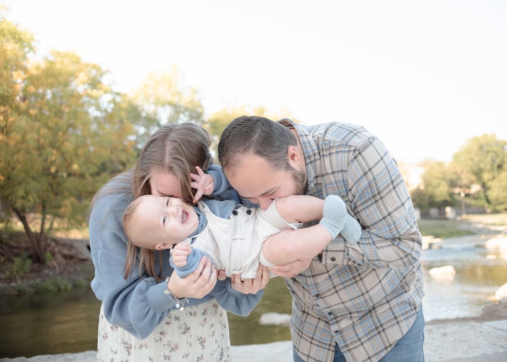 Parents kissing their baby boy during family photos at Nolan Creek in Temple Texas with warm evening light