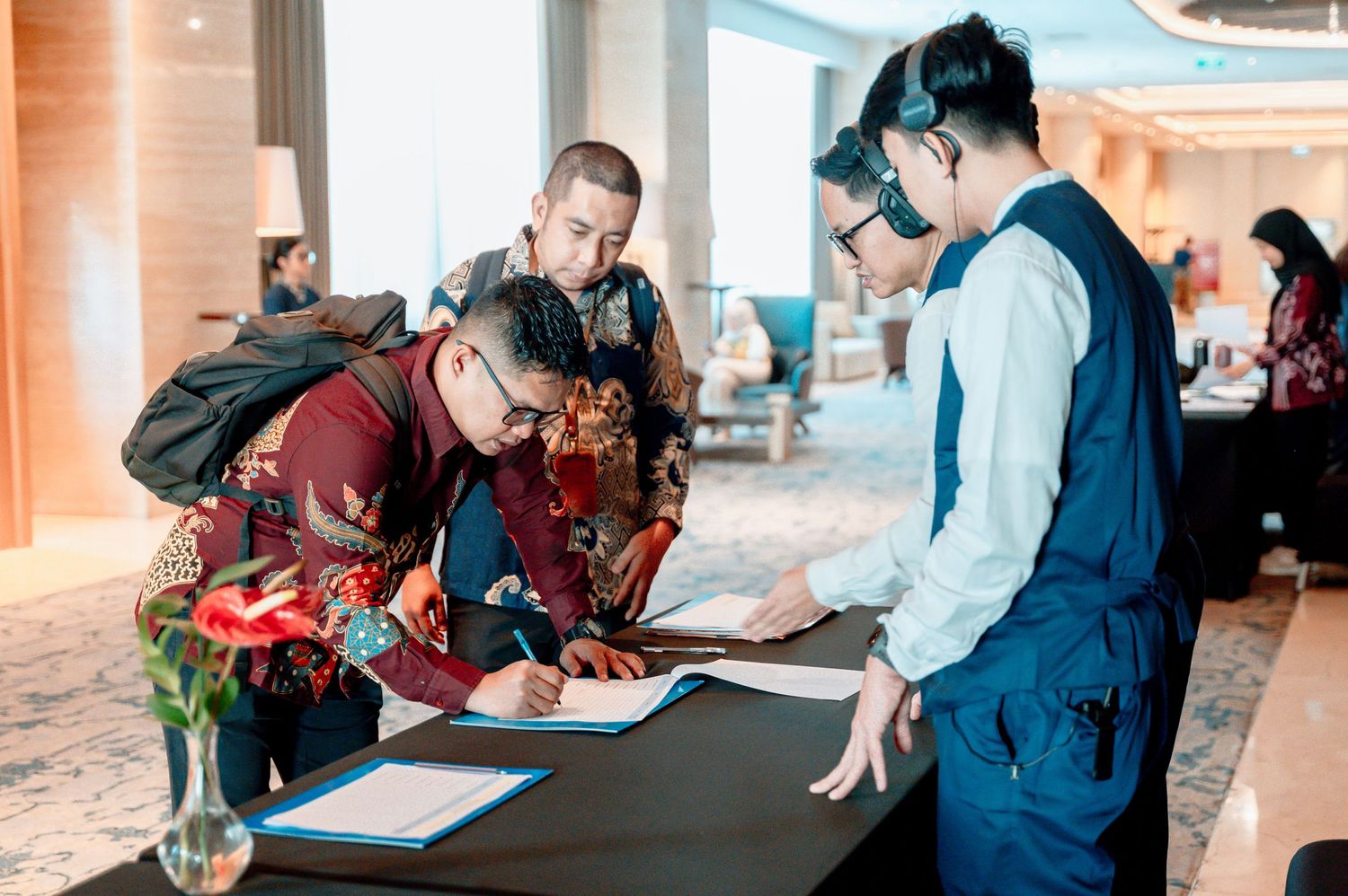 People in traditional attire signing documents at a hotel registration desk during a formal event.