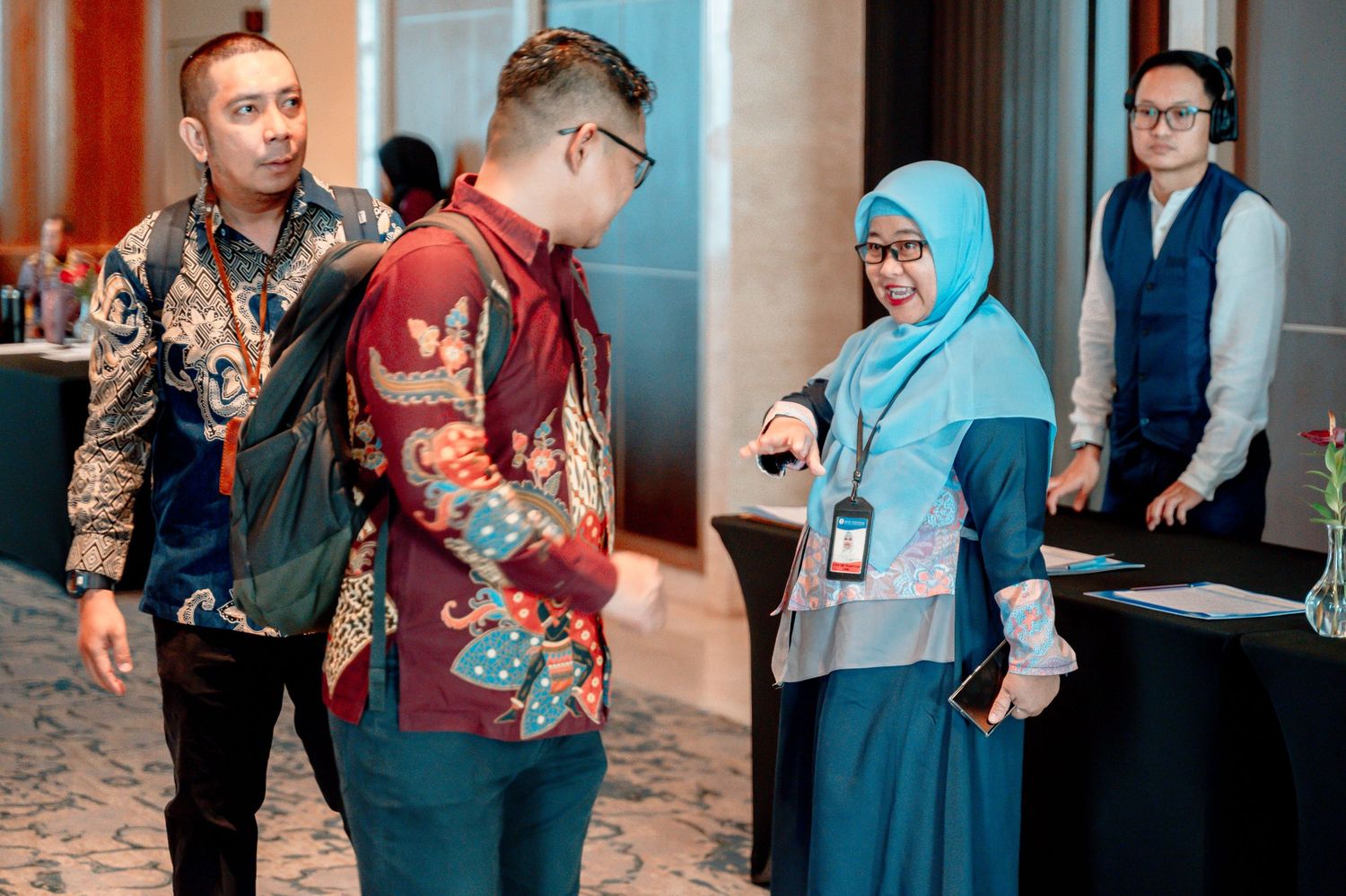 Professionals in batik shirts networking at a formal corporate event in a modern conference hall.