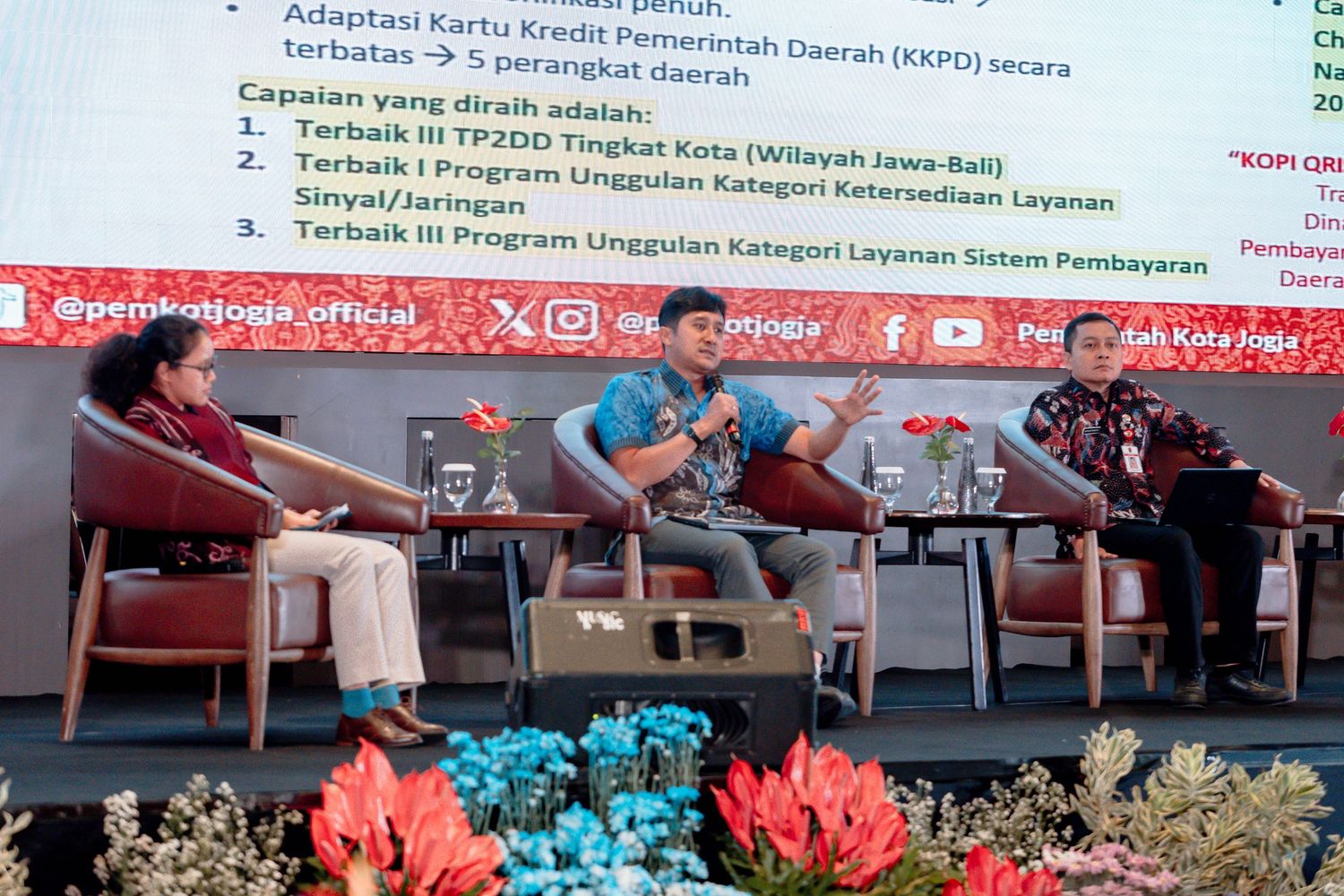 Panel discussion at a government event in Yogyakarta, Indonesia, with speakers seated at a table displaying regional achievements.