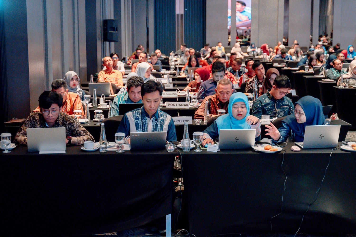 Large conference room filled with attendees working on laptops during a professional seminar or workshop event.