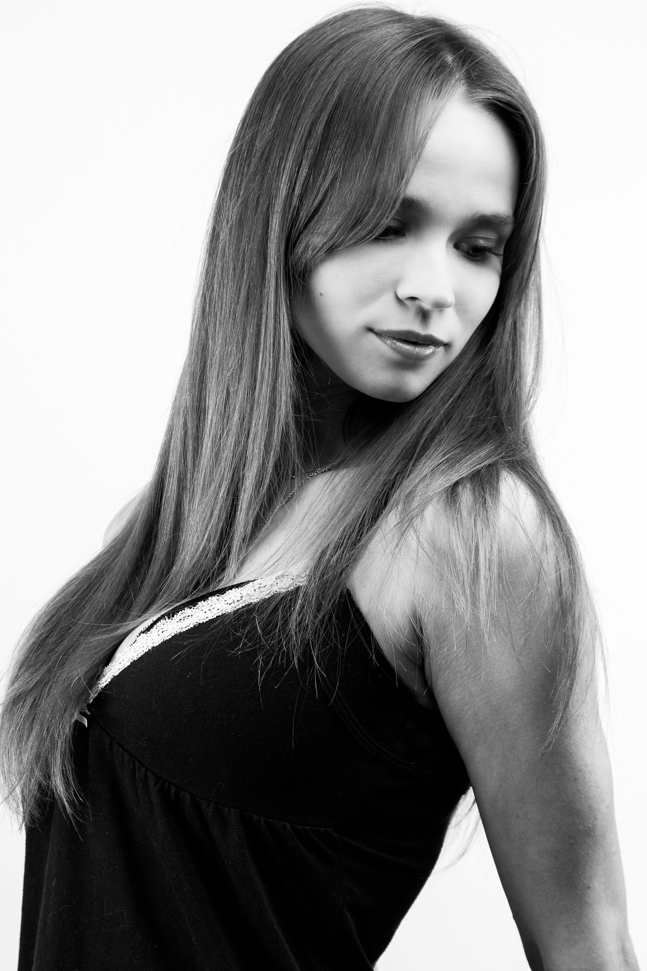 Black and white image of a girl in a black tank top, looking over her shoulder and down