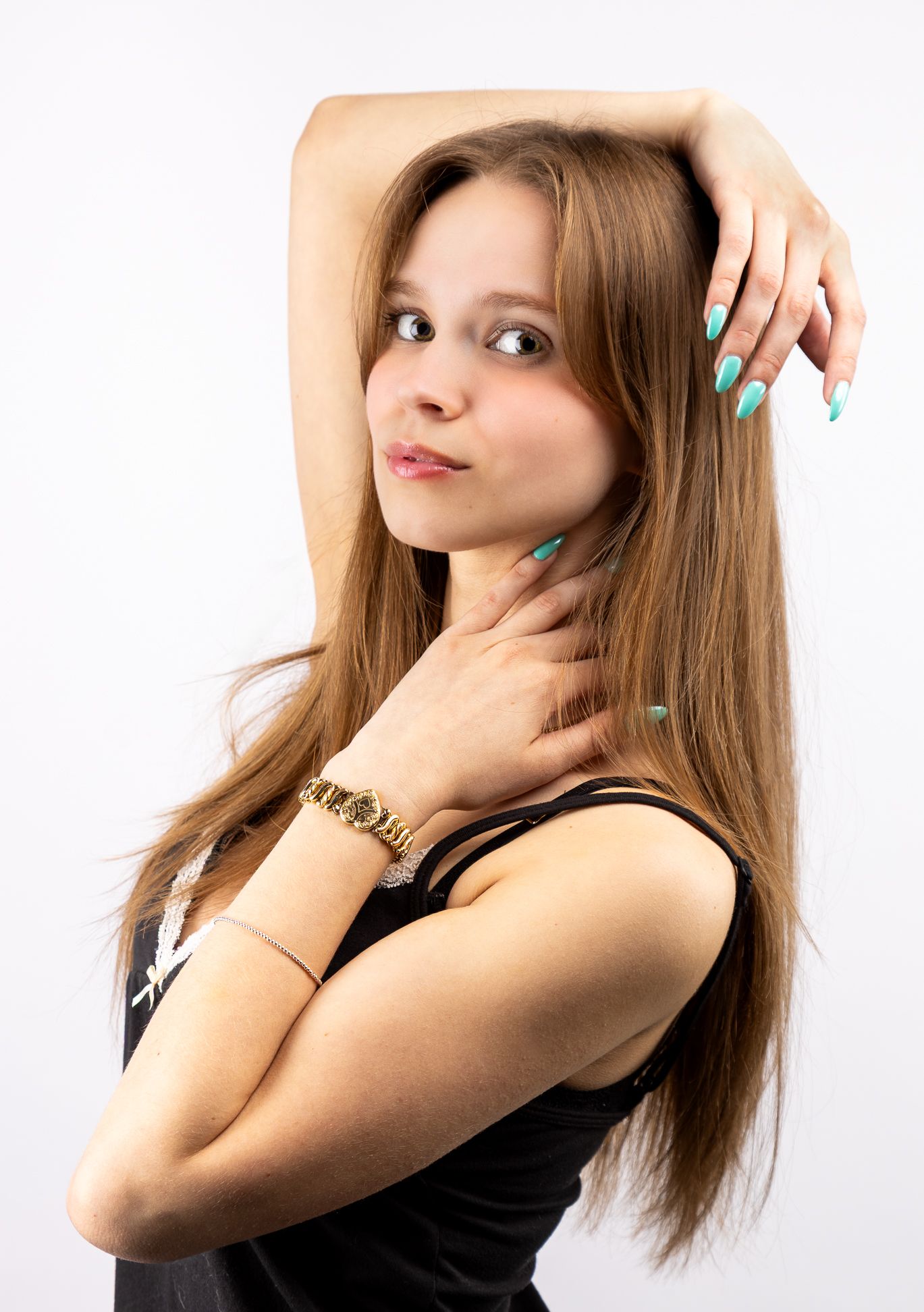 A girl in a black tank top with one arm resting on her head, the other on her neck, looking at the camera from the side