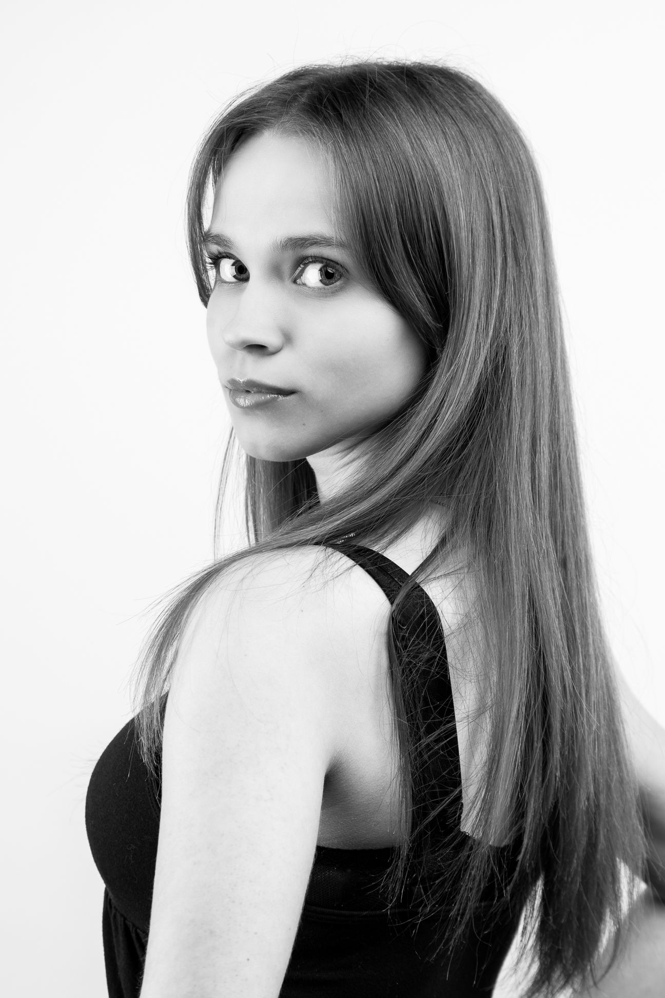 Black and white image of a girl in a black tank top, looking over her shoulder at the camera