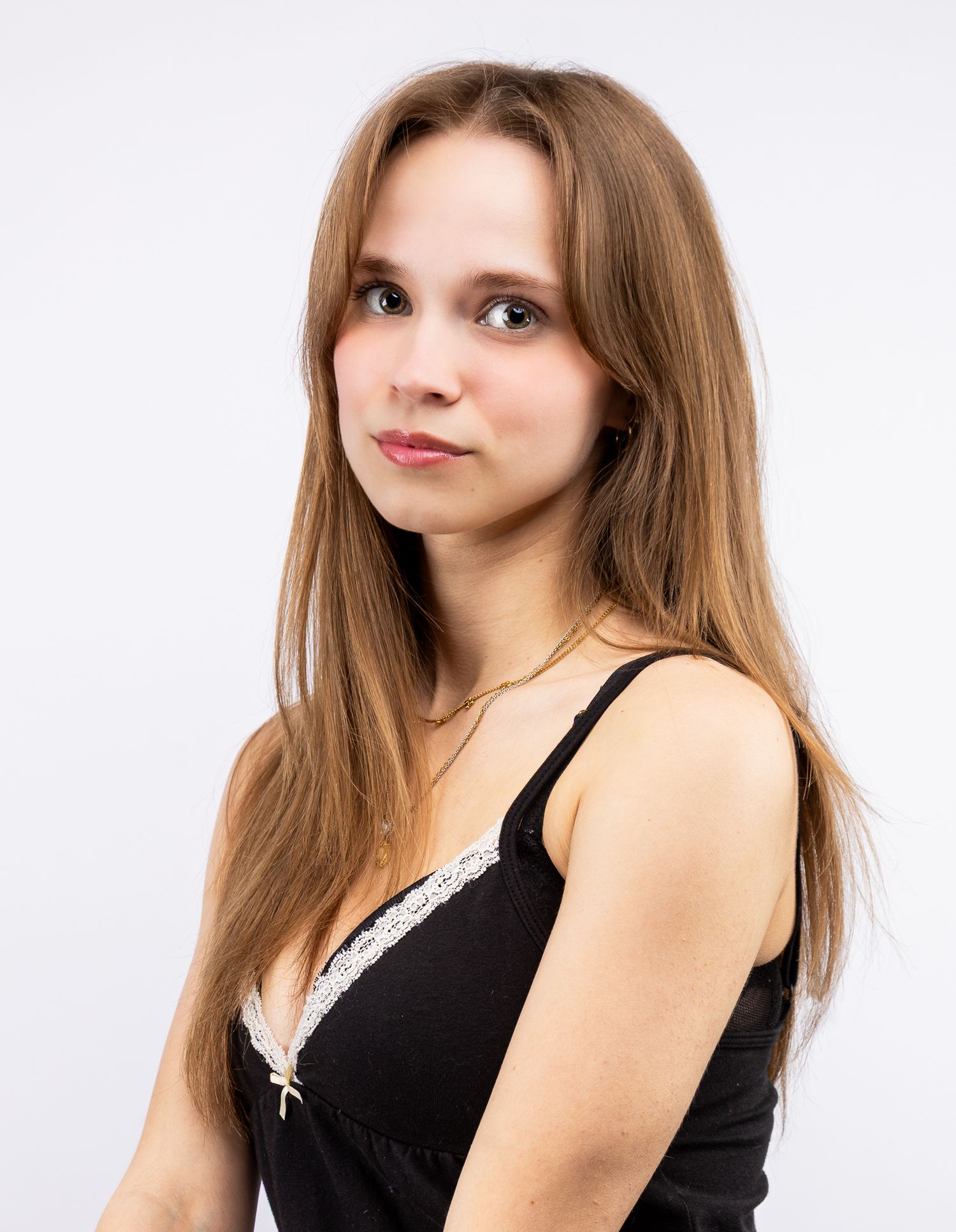 A girl looking at the camera in a black tank top in front of a white backdrop