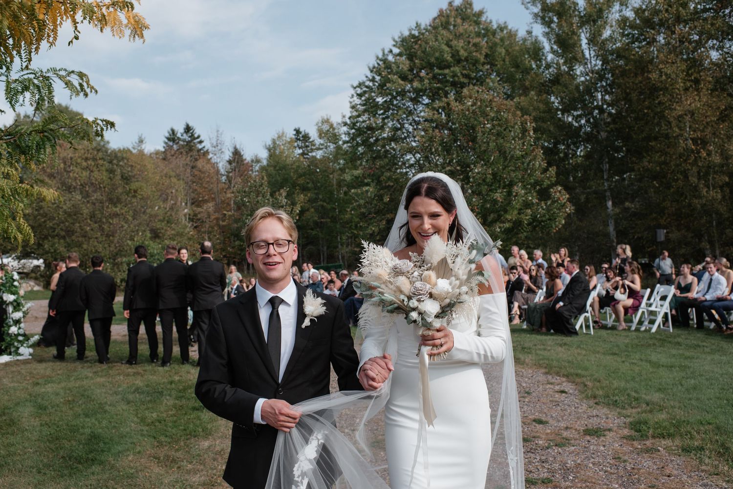 Black and white photo of a bride and groom standing in a lush forest meadow on their wedding day.