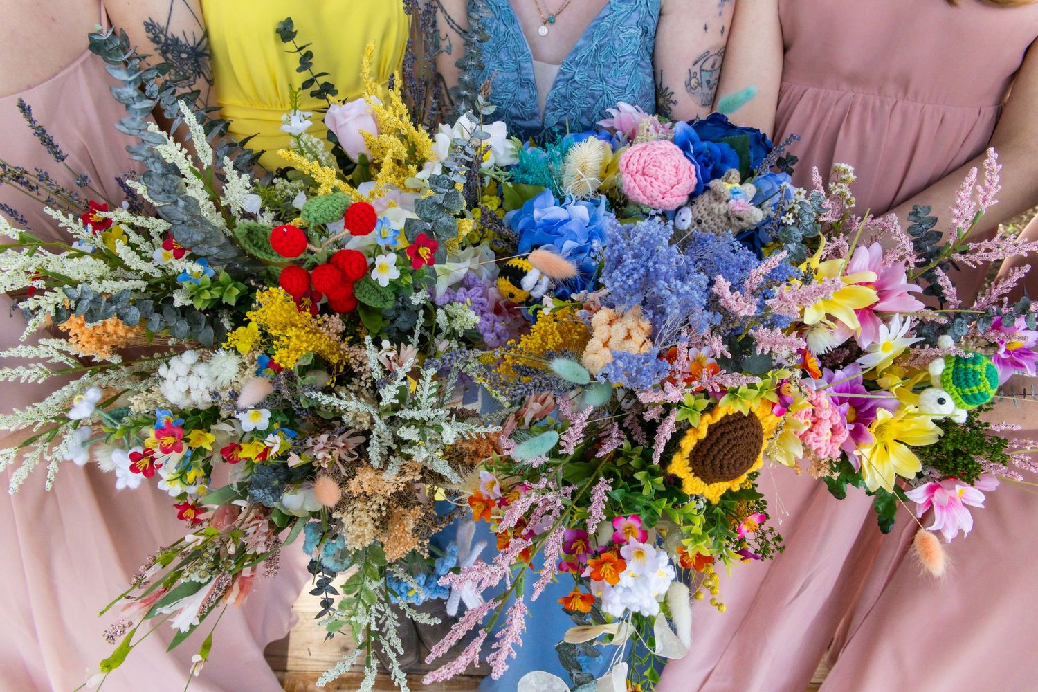 Three bridesmaids holding vibrant wildflower bouquets with sunflowers and colorful blooms.