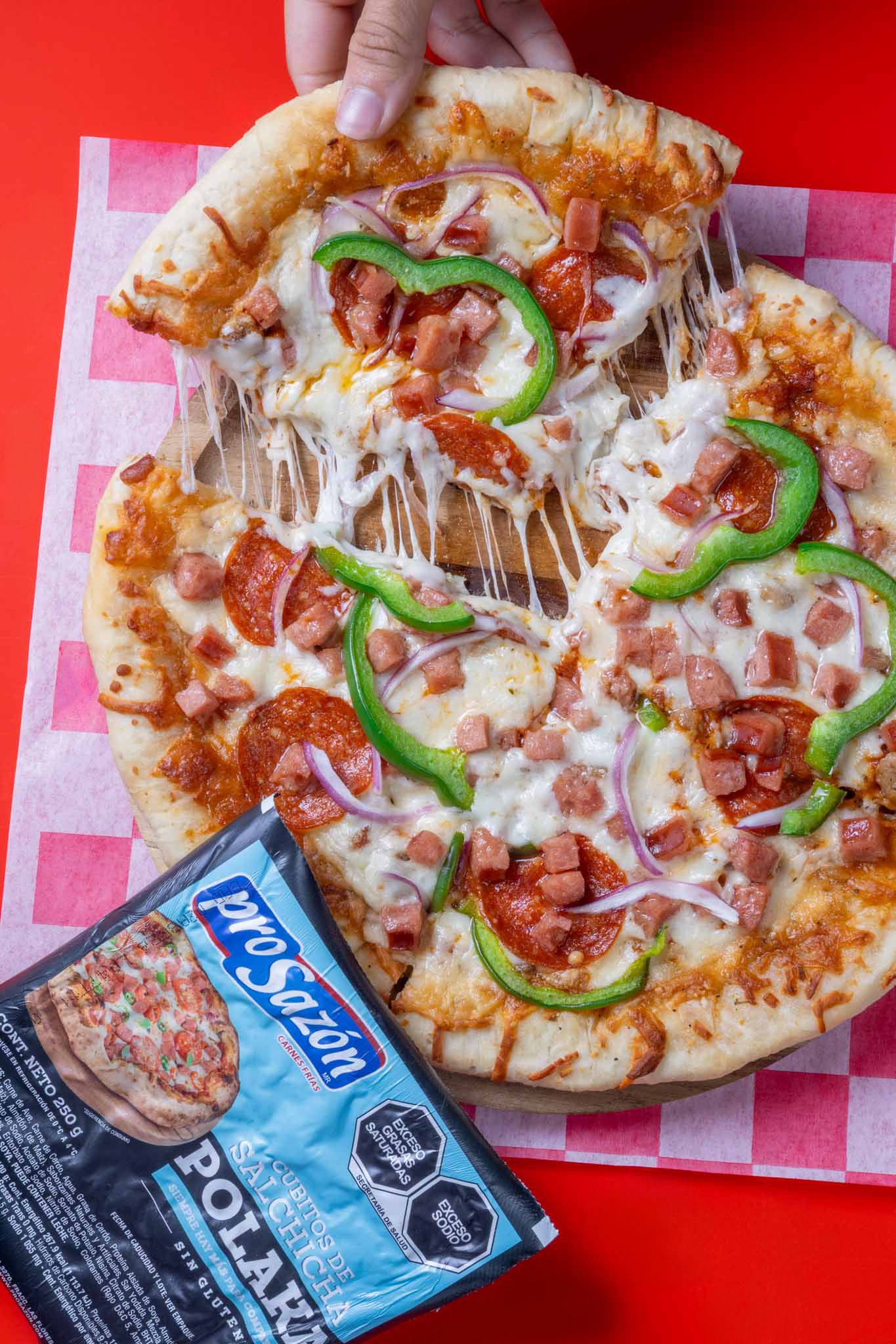 A delicious pizza topped with pepperoni, ham, green peppers, and onions next to a ProSazon Polaka seasoning packet.