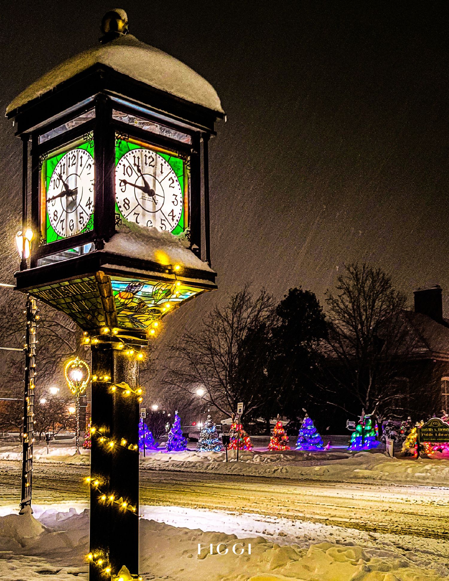 Snow-covered street clock adorned with Christmas lights glows warmly at night during a winter snowstorm with colorful holiday displays.