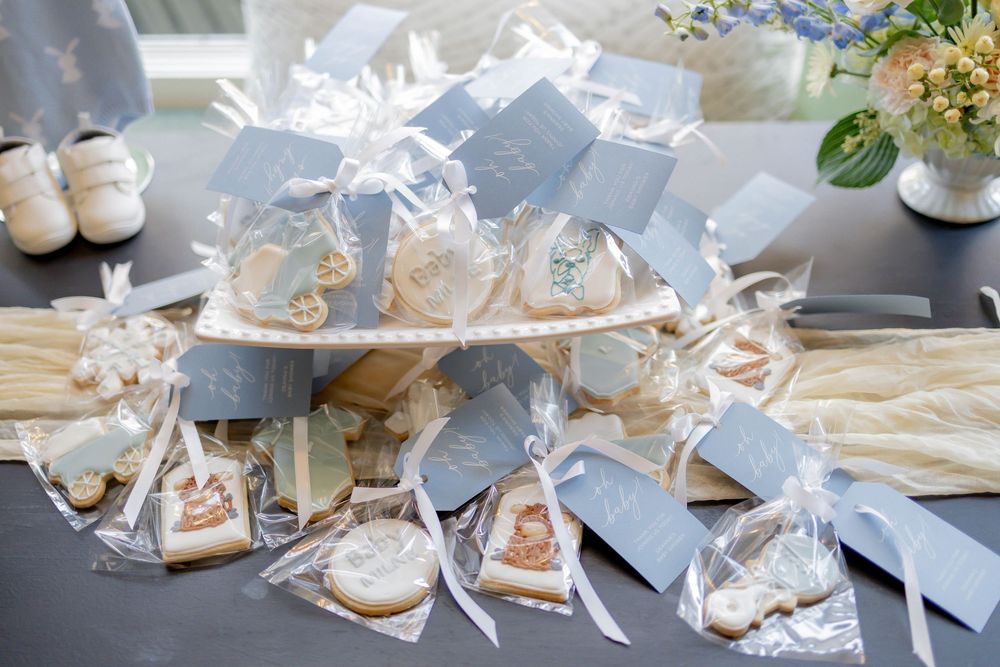 Elegant baby shower favor table with blue-tagged cookies in clear bags and cake pops on a tiered stand.