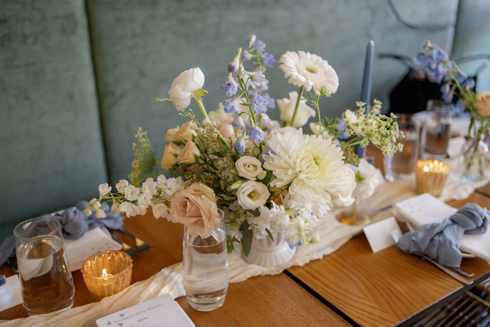 Elegant wedding table centerpiece with white and blue flowers, candles, and place settings on a wooden table.