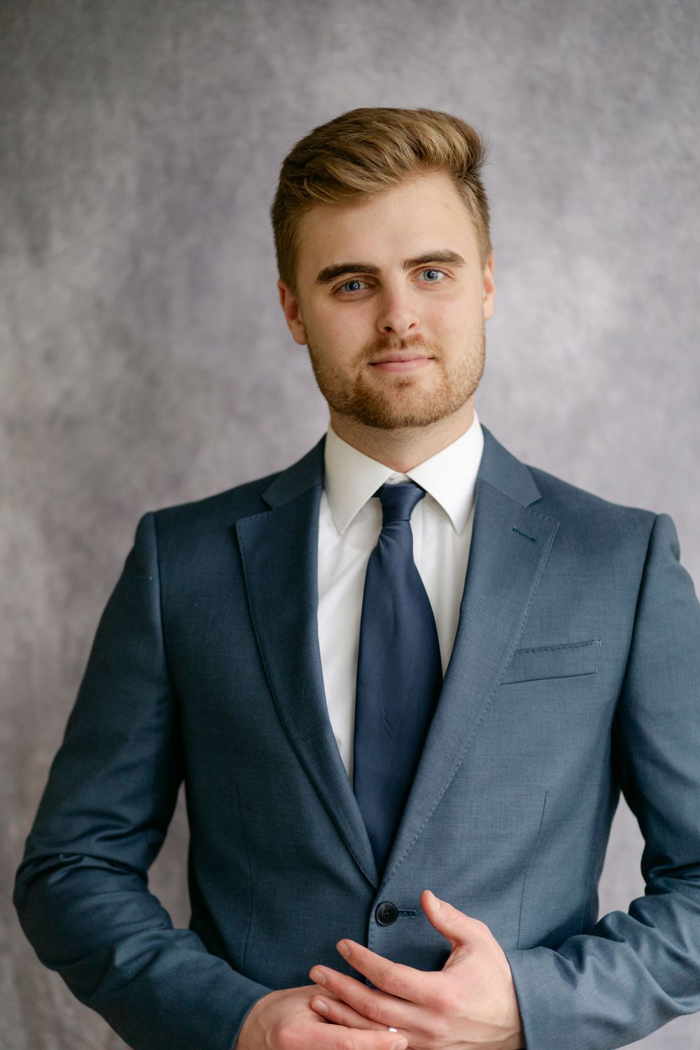 Handsome young groom in blue suit and navy tie poses confidently in studio portrait.