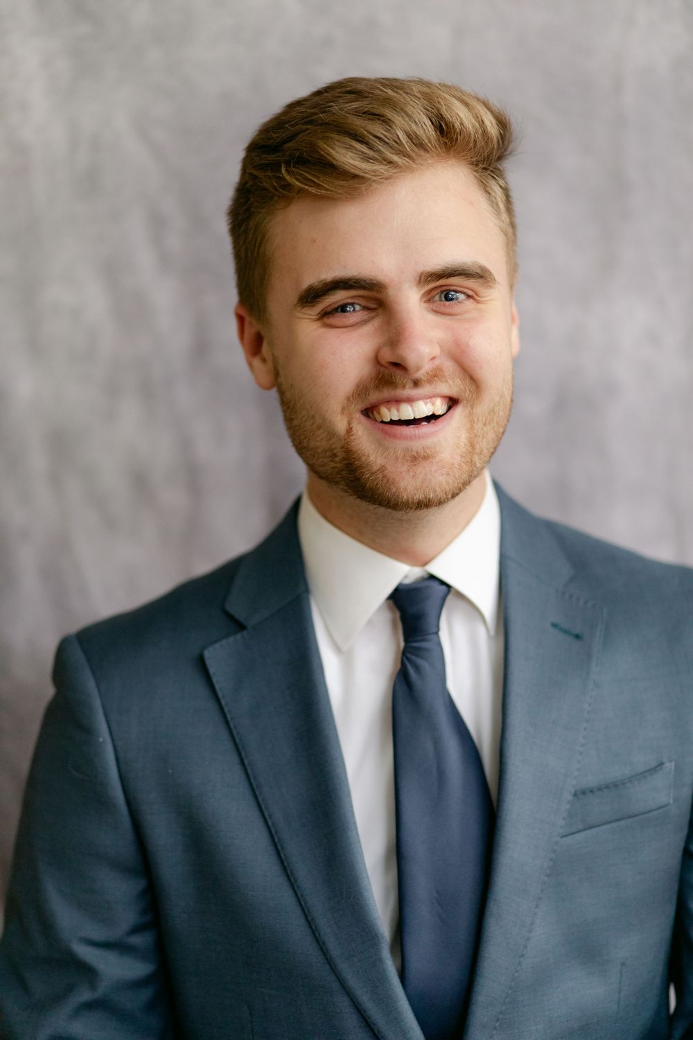 Cheerful young groom in blue suit and navy tie smiles broadly in studio portrait.