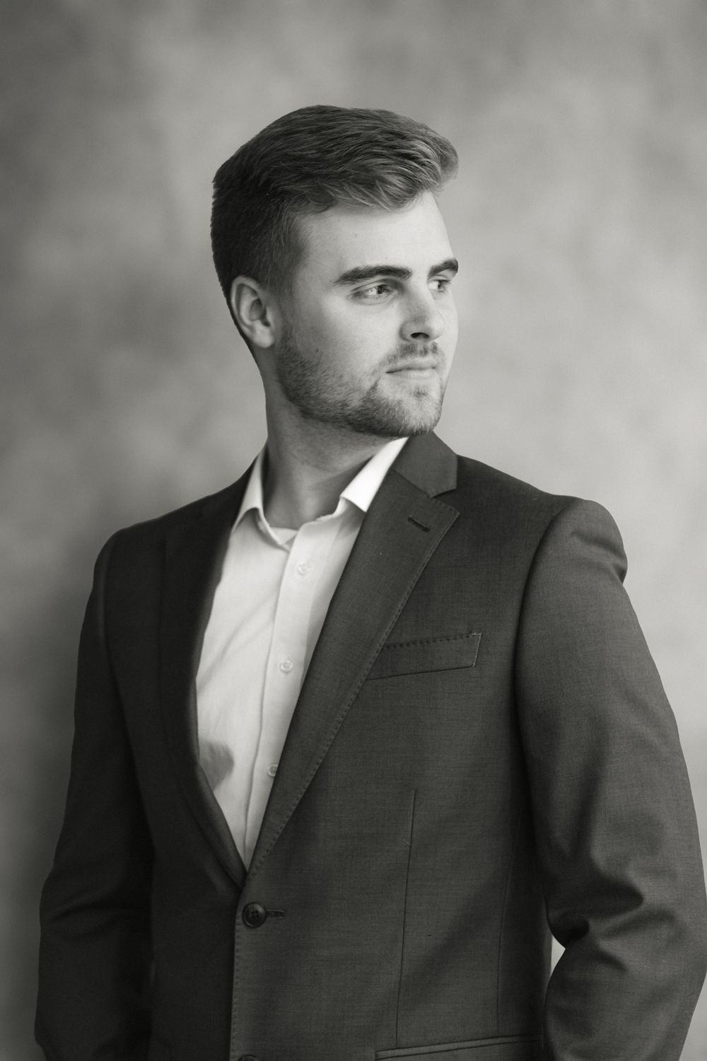 Confident young man in dark suit gazes sideways in elegant black and white studio portrait.