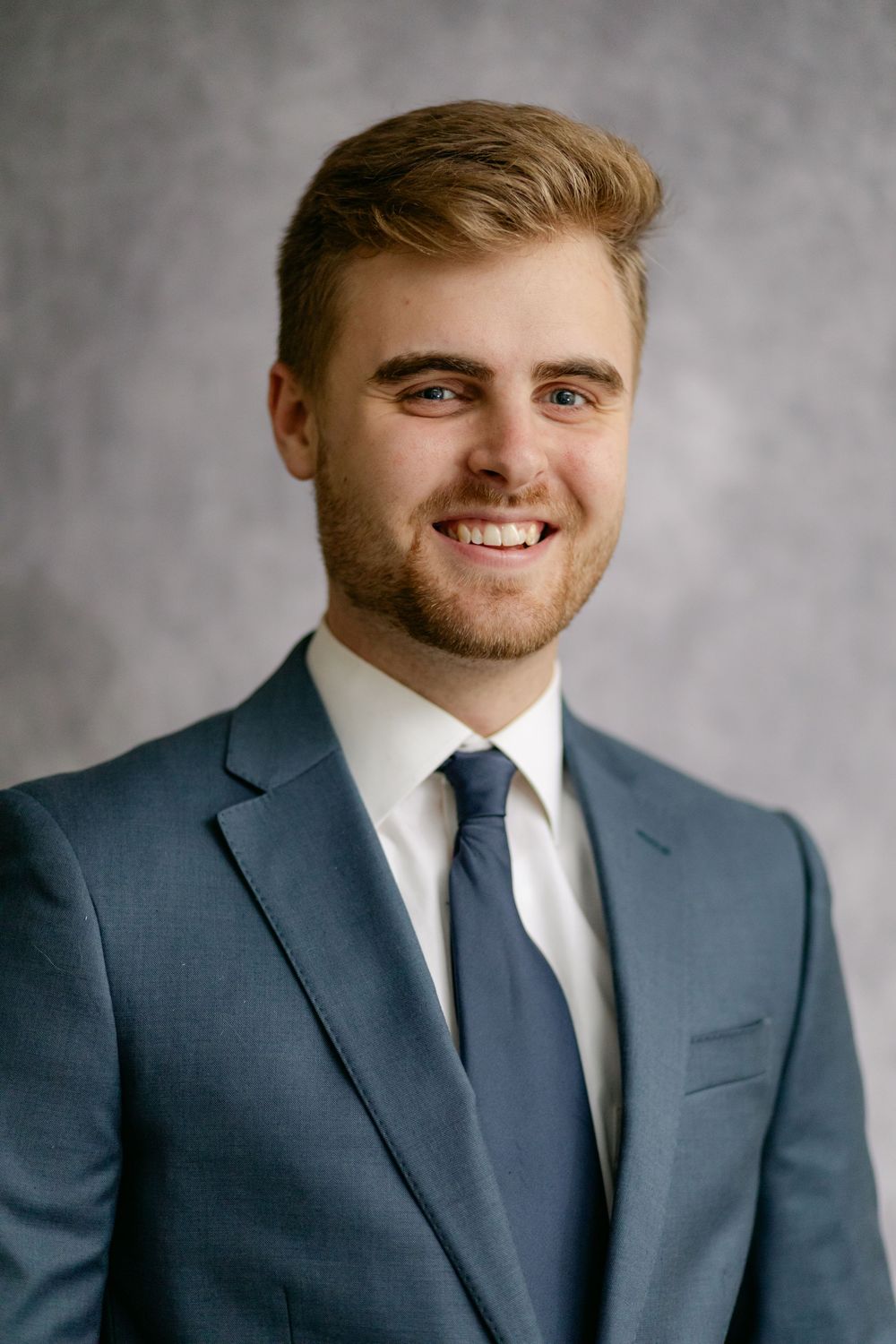 Smiling young groom in blue suit and navy tie poses in bright studio portrait.