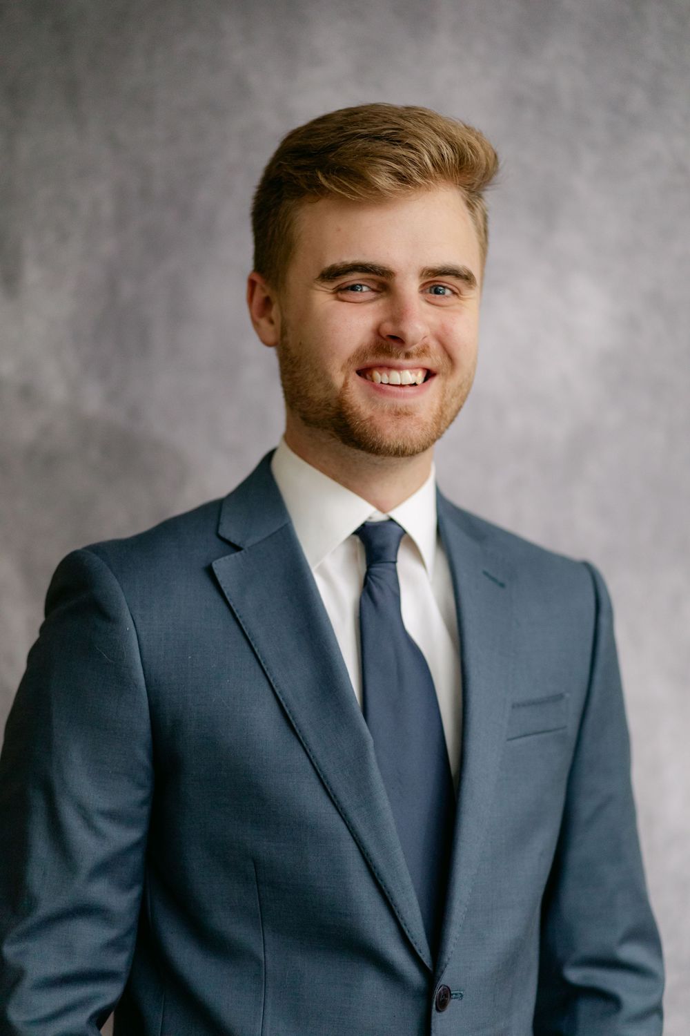 Happy young groom in blue suit and navy tie smiles warmly in studio portrait.