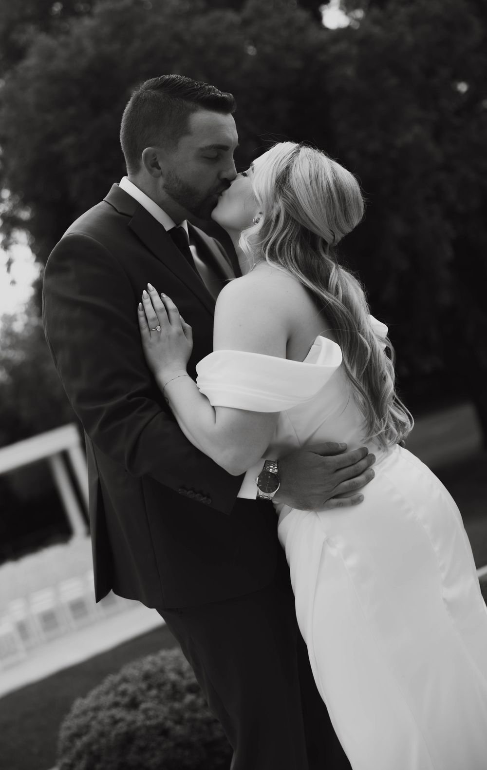 Black and white photo of bride and groom sharing a passionate kiss outdoors at their wedding.
