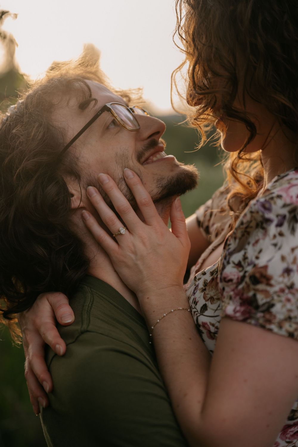 A couple shares a romantic moment at sunset, woman holding man's face as he smiles up at her in golden light.