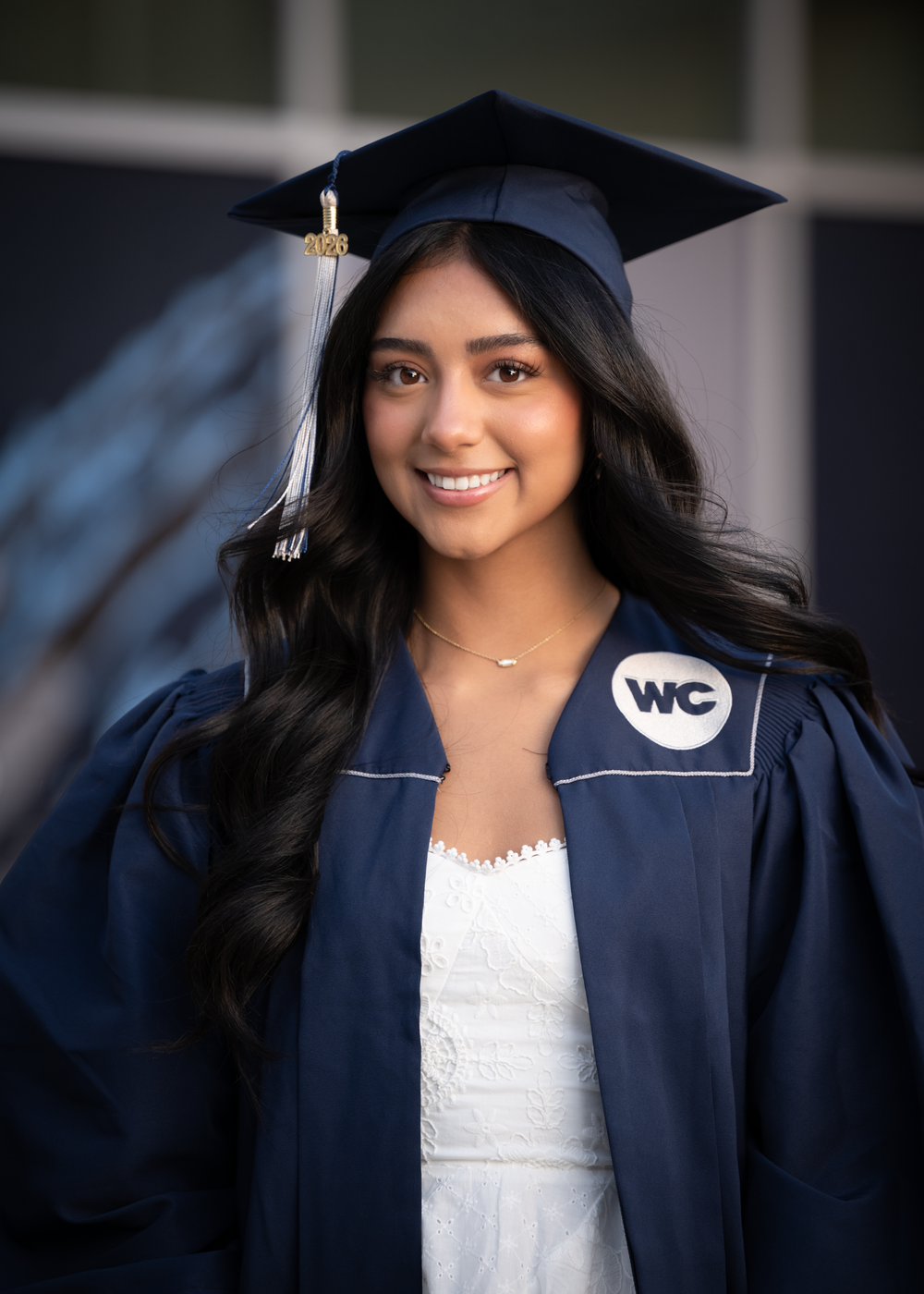 Smiling graduate in navy cap and gown with WC emblem poses for portrait photo.