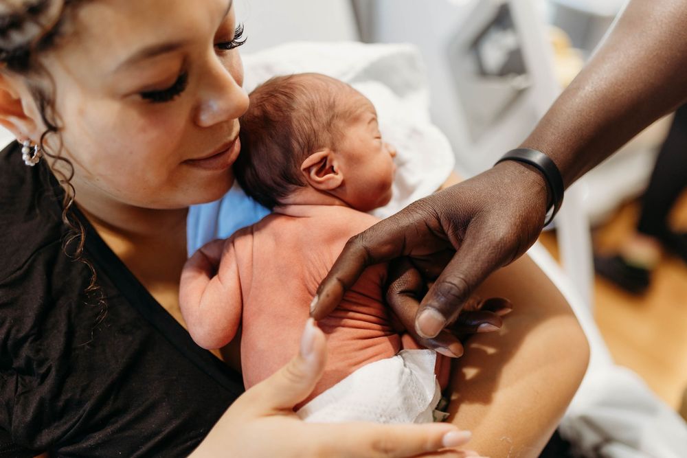 A mother tenderly holds her newborn baby while a doctor checks the infant shortly after birth.