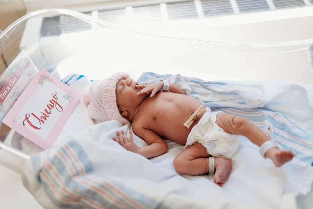 A newborn baby rests in a hospital bassinet with a pink name tag reading Chicago.