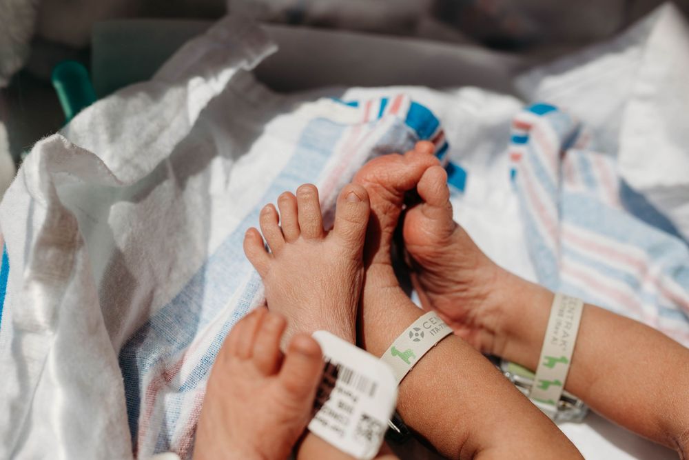 Adult hand gently holding newborn baby feet with hospital ID bracelet in maternity ward.