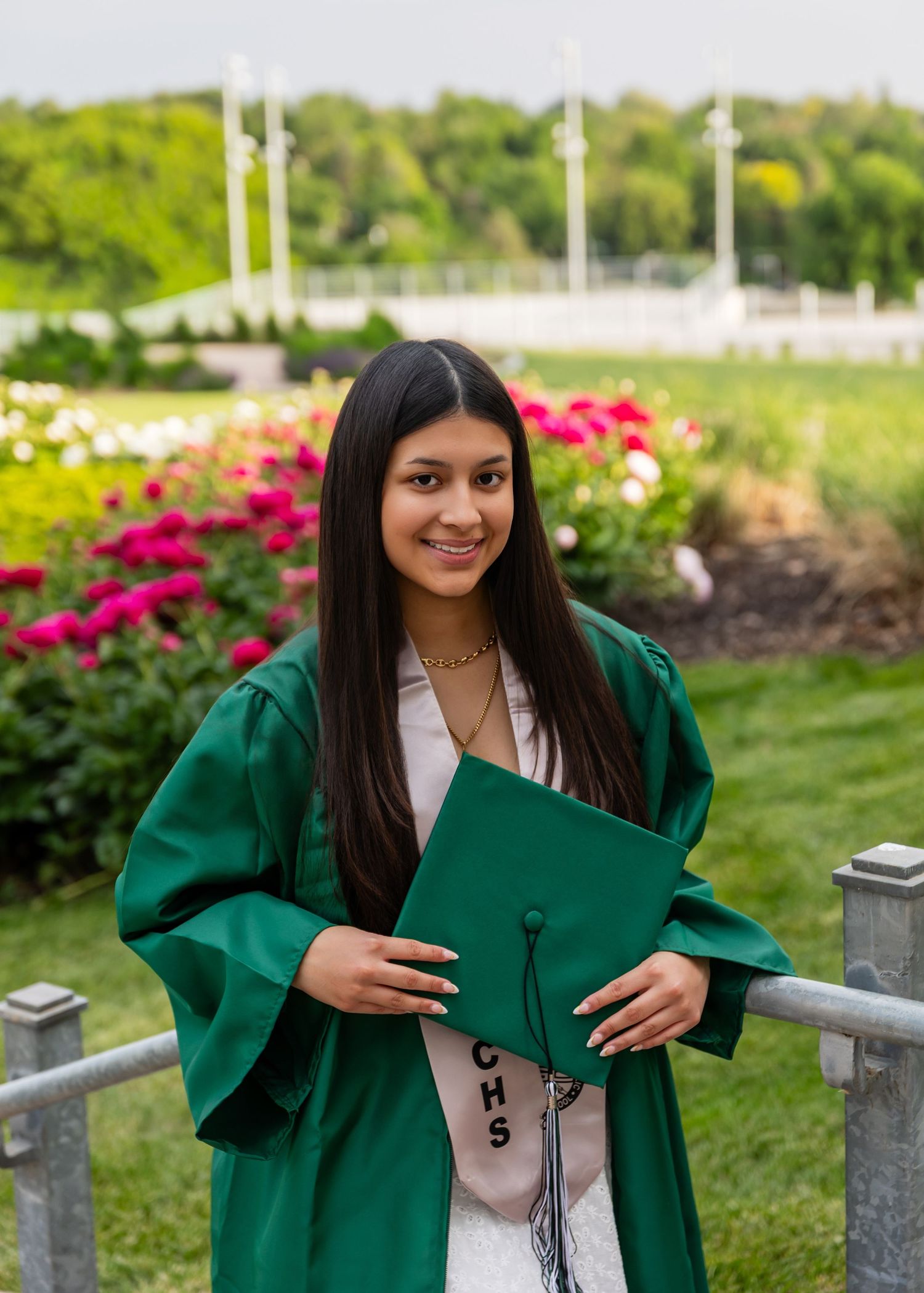 Young Skutt Catholic girl graduate in green graduation gown and cap smiles outdoors at Memorial Park in Omaha.