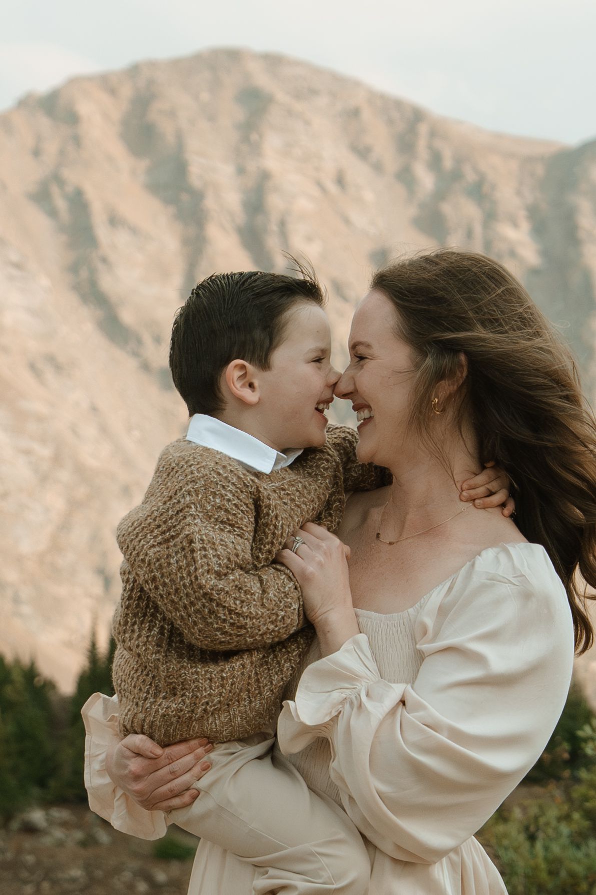A mother holds her young son as they share a sweet nose-to-nose moment with a mountain backdrop.