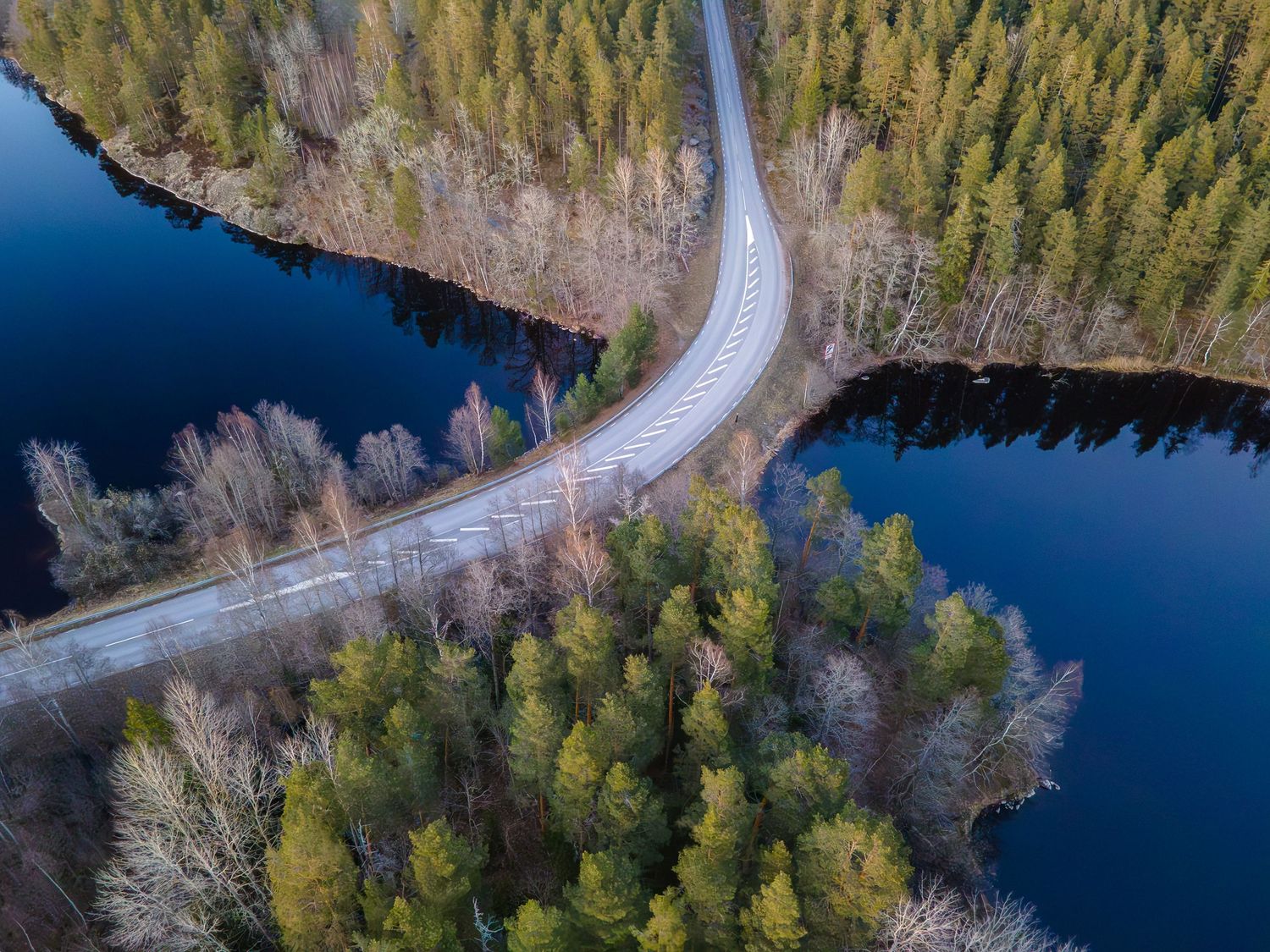 Bild från drönare som visar en asfaltsväg som passerar en sjö genom ett skogslandskap.