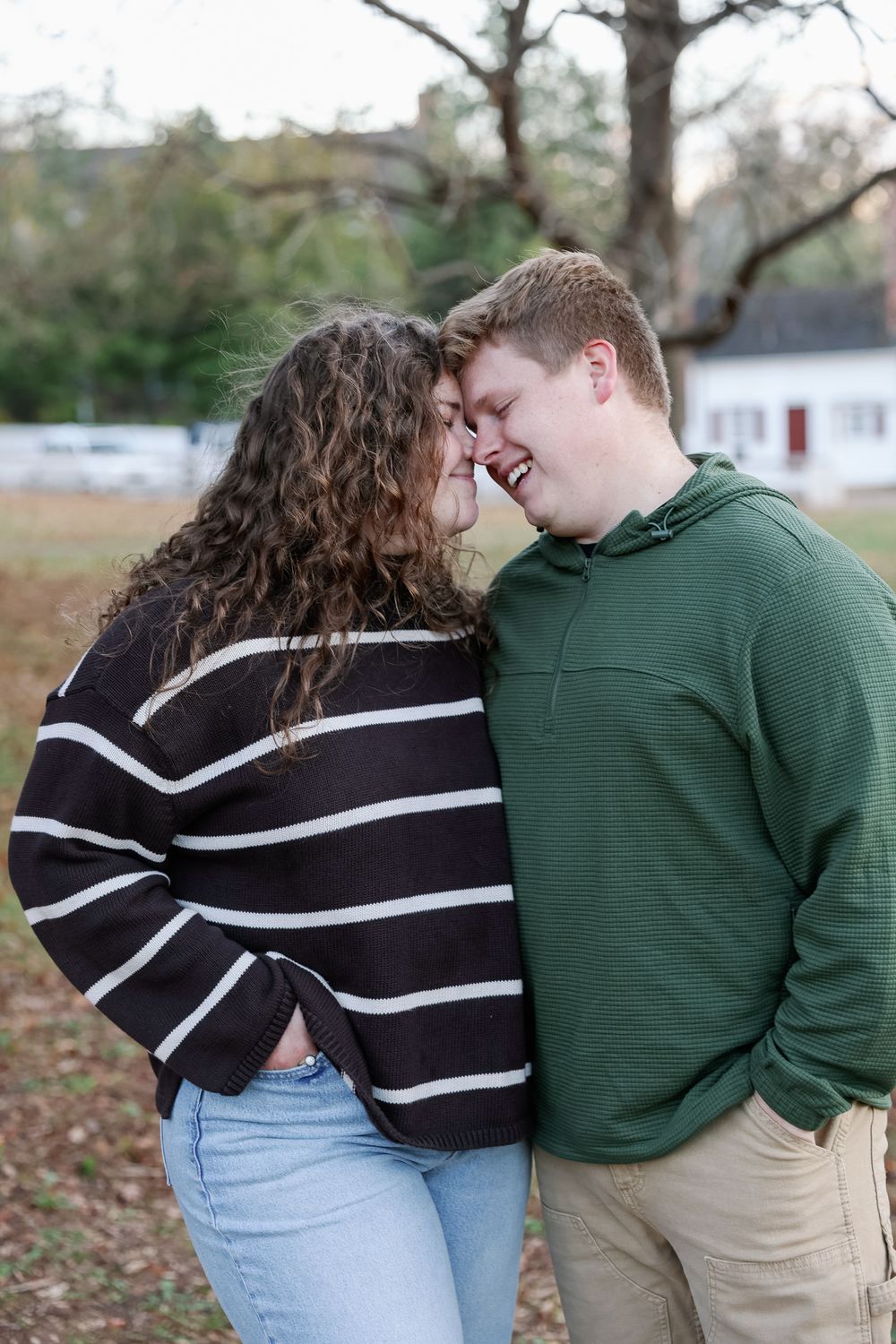 A young couple in casual attire share a tender forehead-to-forehead moment outdoors, smiling warmly at each other.