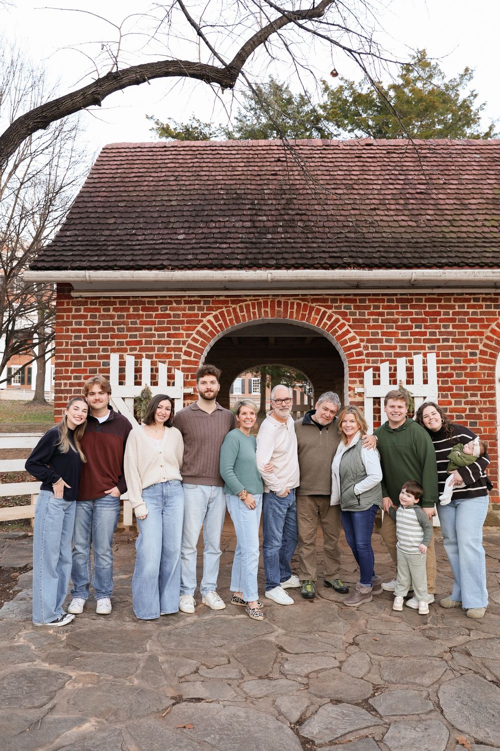 Large family group portrait outdoors in front of a rustic brick archway building during winter.
