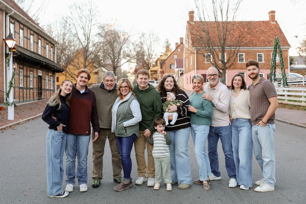 A large family group poses together smiling outdoors in a charming village setting during fall.
