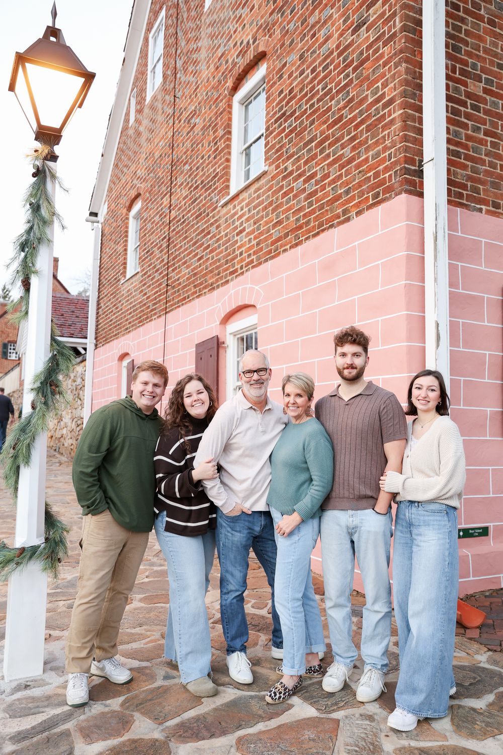 Happy family of six posing together outdoors near a brick building decorated with holiday greenery.