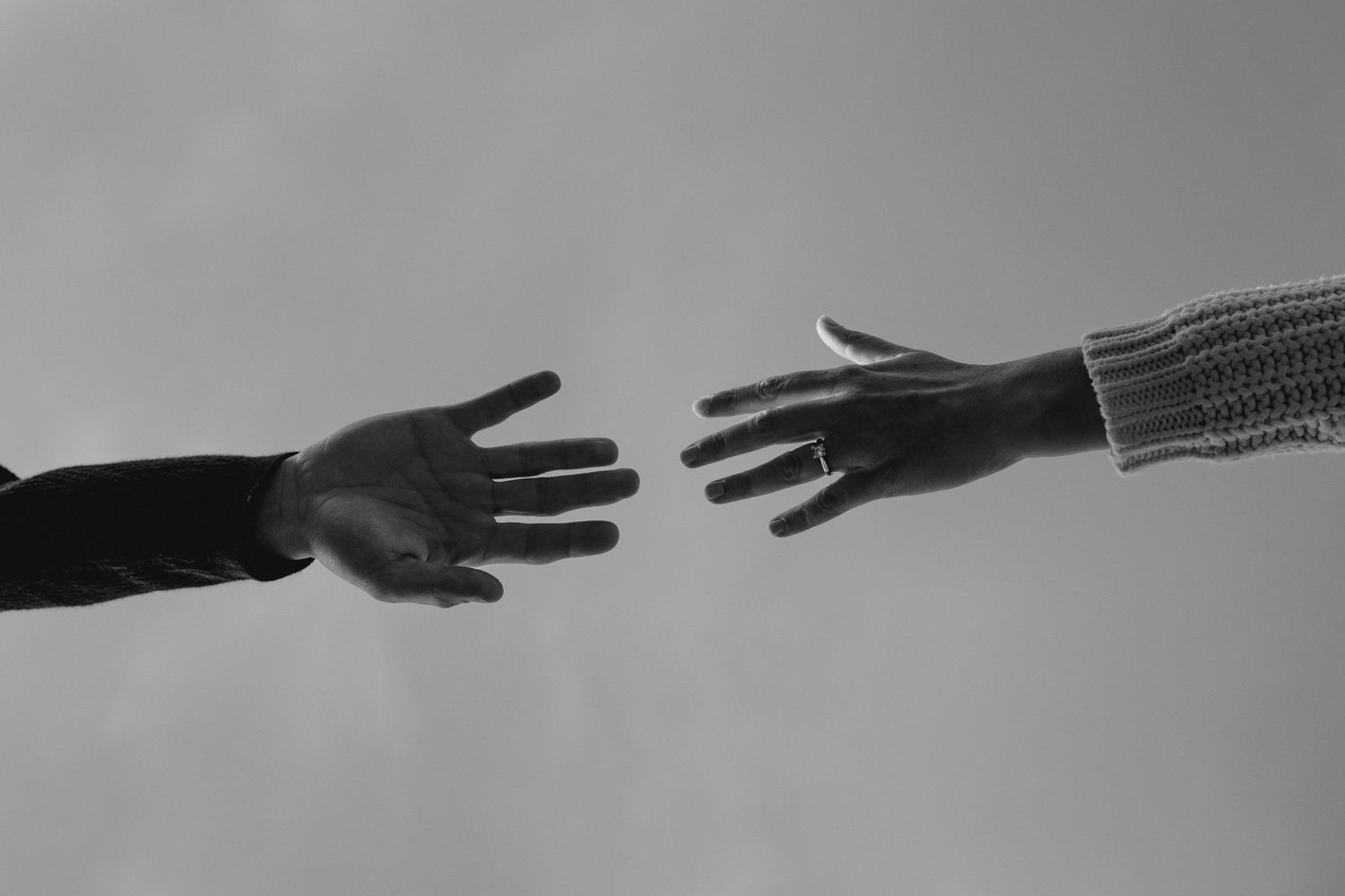 Two hands reaching toward each other in a black and white photo, symbolizing connection and support.