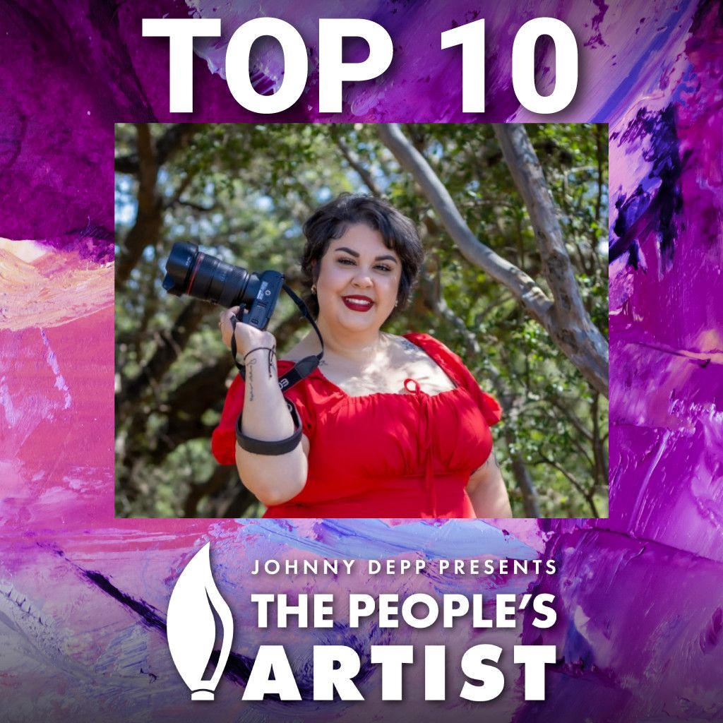 Isis Olguin, a photographer in a red dress, smiles while holding a camera outdoors among trees.