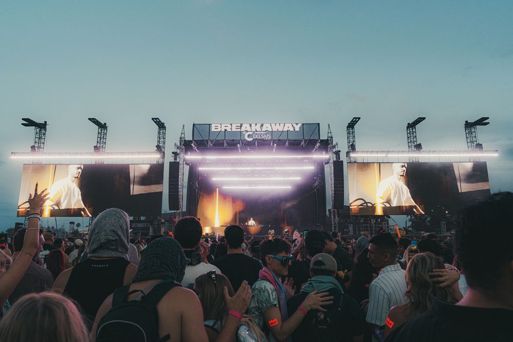 Crowd enjoying Breakaway Music Festival at an outdoor stage with bright lights at dusk.