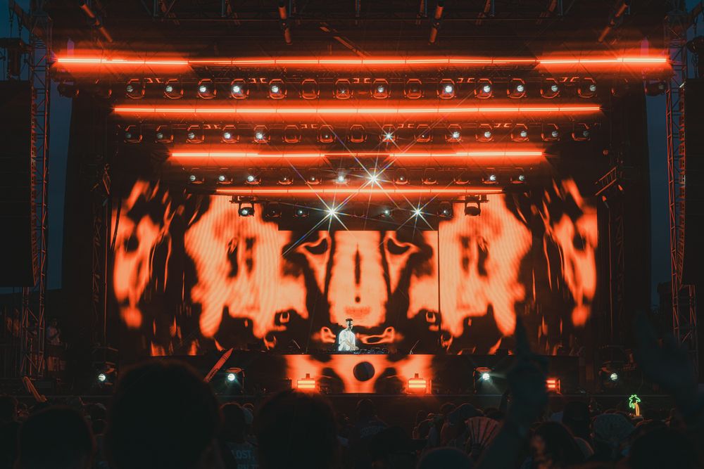 DJ performs on stage with dramatic red neon lights and fiery visual effects at an electronic music concert.