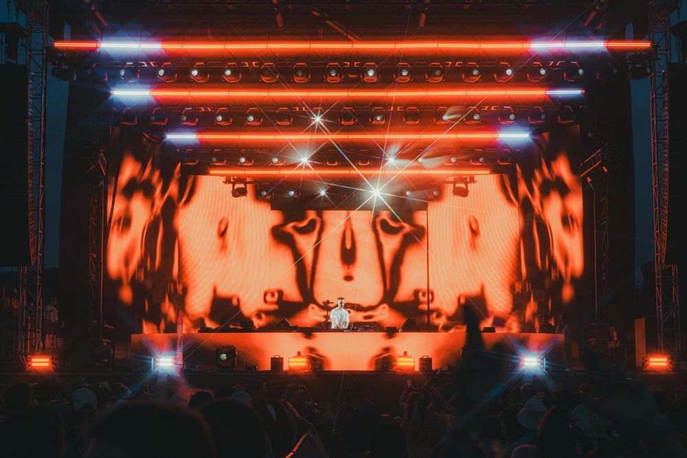 DJ performing on a vibrant stage with orange LED lights and dynamic visual displays at a live music event.