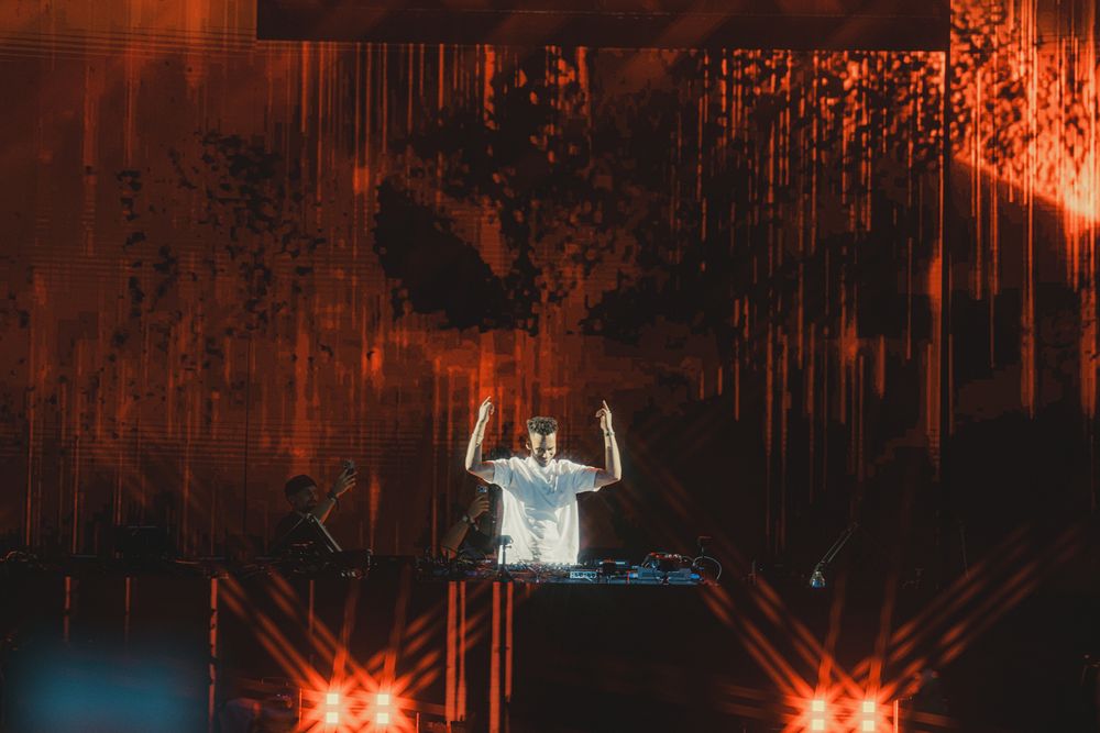 DJ performing on stage with dramatic red and orange lighting at a live event.