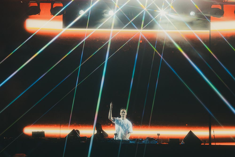 DJ performing on stage with colorful laser light show beams at a live concert event.