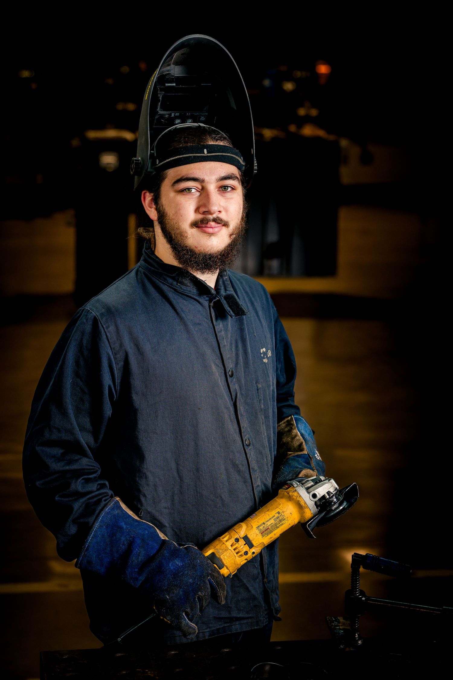 A young welder in protective gear stands confidently in a Pearland Welding workshop holding welding equipment.