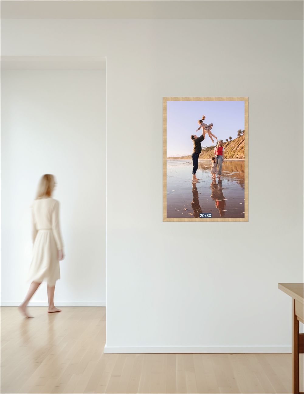 A single gold-framed beach family photo of parents lifting a child, displayed on a bright white hallway wall.