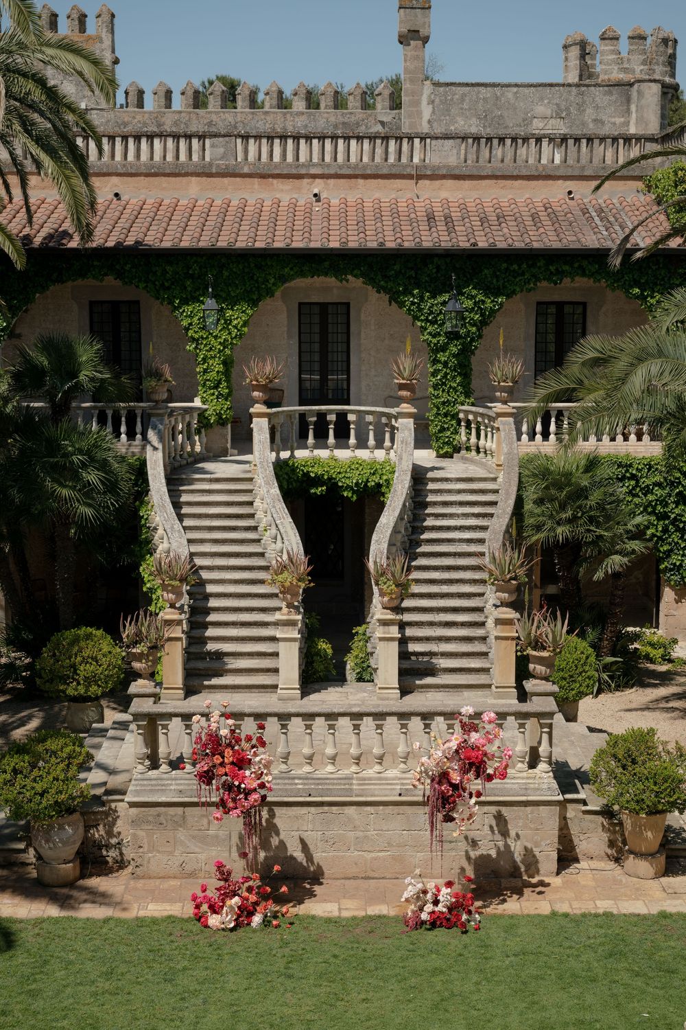 Elegant stone staircase with pink floral arrangements at an ivy-covered Mediterranean villa with terracotta roof.