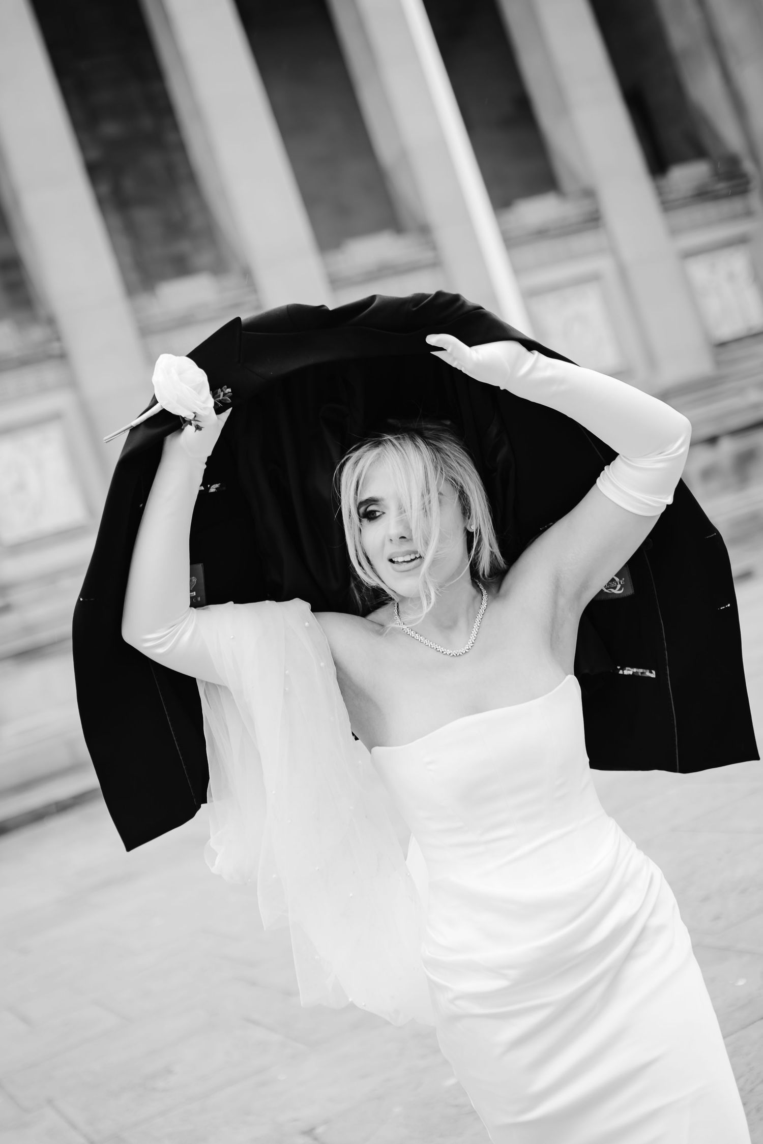Black and white photo of a bride in a wedding dress and veil flowing in an elegant indoor setting.