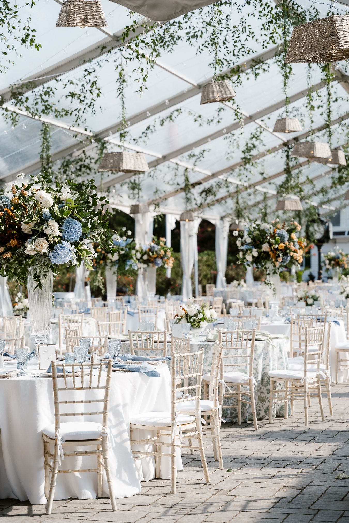 Bride in white off-shoulder gown and groom in white tuxedo share a romantic moment on a balcony overlooking scenic countryside.